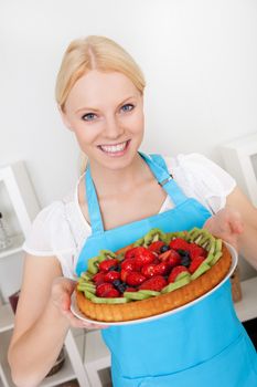 Beautiful young woman holding self-made cake in the kitchen