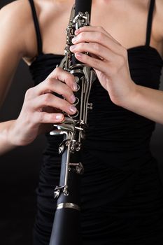 Beautiful young woman playing clarinet over black background