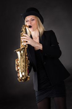 Beautiful young woman playing saxophone over black background