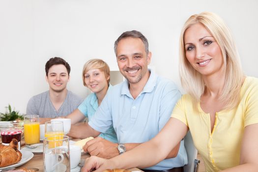 Happy family with two teenage children sitting around the table enjoying a healthy breakfast