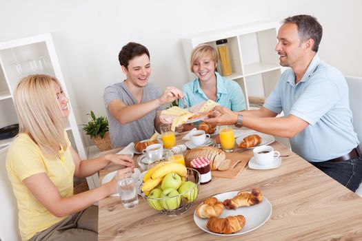 Happy family with two teenage children sitting around the table enjoying a healthy breakfast