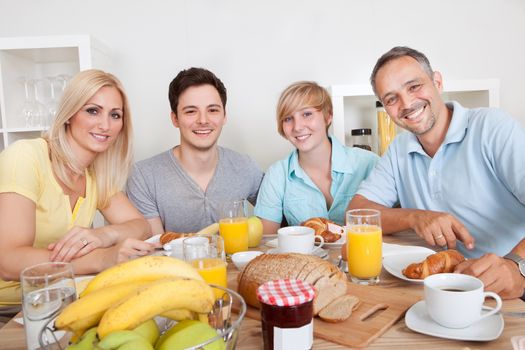 Happy family with two teenage children sitting around the table enjoying a healthy breakfast