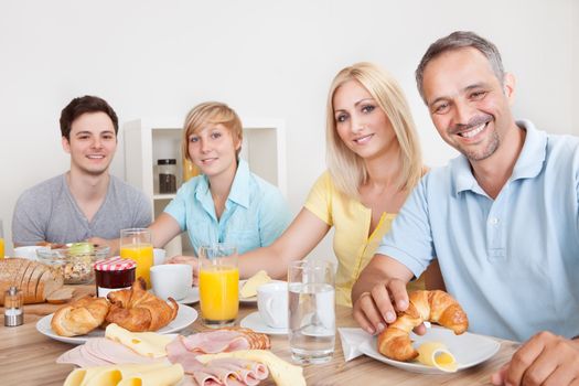 Happy family with two teenage children sitting around the table enjoying a healthy breakfast