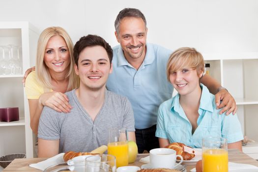 Happy family with two teenage children sitting around the table enjoying a healthy breakfast