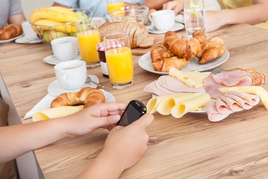 Close-up on teenager texting on her mobile phone in the kitchen while the rest of the family enjoy breakfast