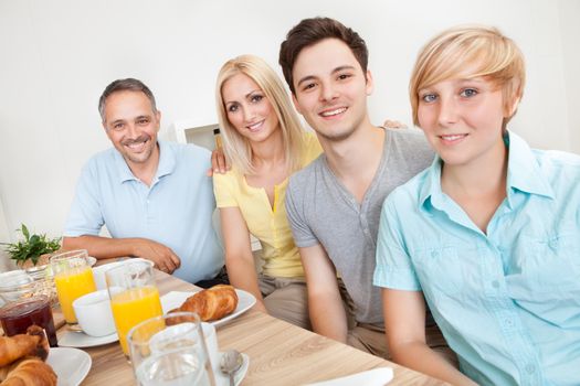 Happy family with two teenage children sitting around the table enjoying a healthy breakfast