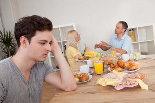 A young teenage son looks very downhearted and despondent at her parents who are arguing in the background