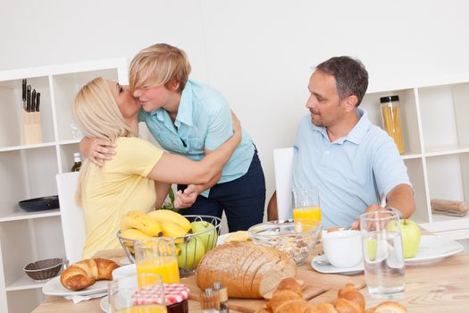 Mother and daughter enjoy a hug at the breakfast table watched by the happy proud father
