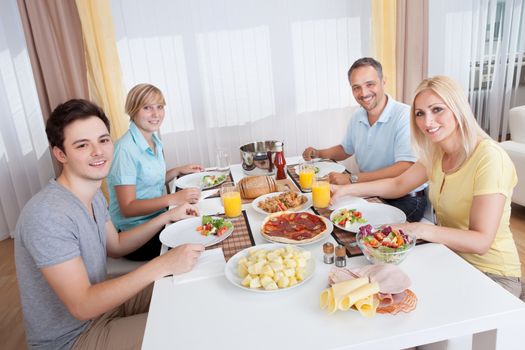 Young happy family with teenage children sitting down to eat a cold lunch of meat and salads