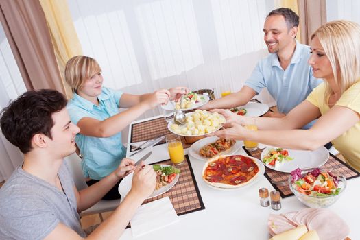 Happy family with a teenage son and daughter seated at the table serving themselves to a healthy cold dinner with meat and salads