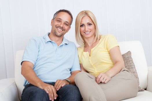 Smiling loving attractive middle-aged couple sitting close together relaxing on a sofa