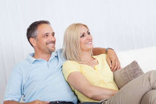 Smiling loving attractive middle-aged couple sitting close together relaxing on a sofa