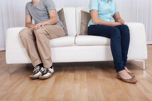 Brother and sister have had an argument and are sitting at opposite ends of a sofa