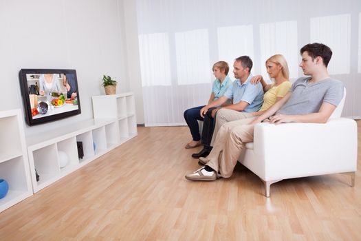 Family with teenage children sitting together on a sofa in the living room watching widescreen television