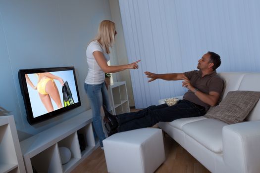 Wife standing blocking the television set and preventing her husband from watching female TV while remonstrating with him