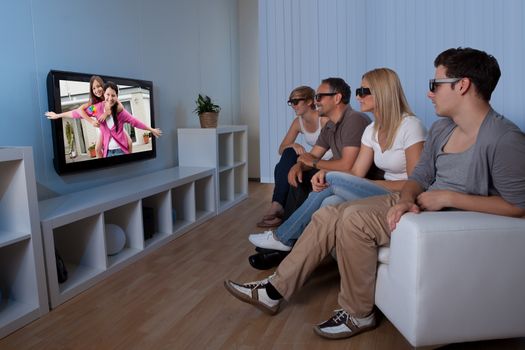 Family with teenage children sitting together on a couch eating bowls of popcorn wearing 3d glasses and watching the television