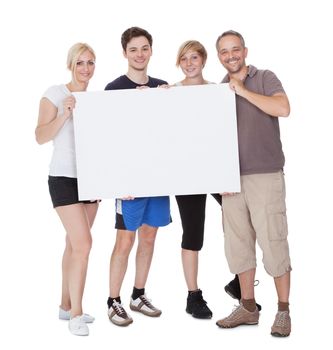 Happy family with two teenage children holding up a blank placard or sign with copyspace for your advertising of announcement