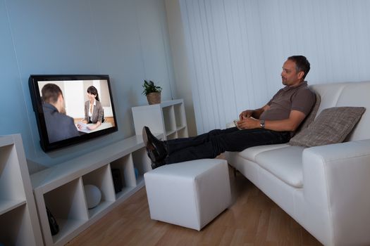 Man recline comfortably on his living room couch watching home movies on his widescreen television set