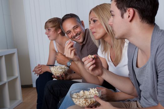 Family with teenage children sitting together on a couch eating popcorn and watching the television
