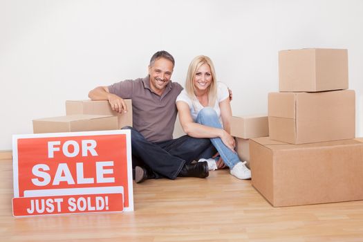 Happy family moving into the new home sitting in an empty room on the floor with small stack of cardboard boxes