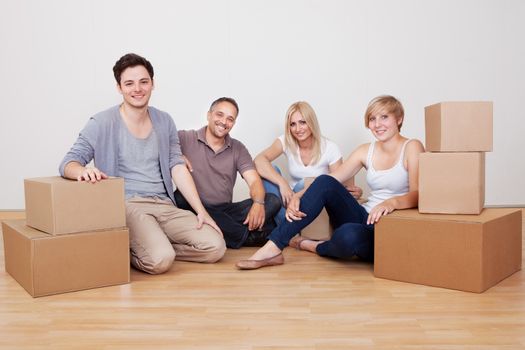 Happy family moving into the new home sitting in an empty room on the floor with small stack of cardboard boxes