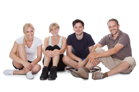 Happy friendly family with a teenage son and daughter lying in a row on the floor on their stomachs relaxing resting on their elbows