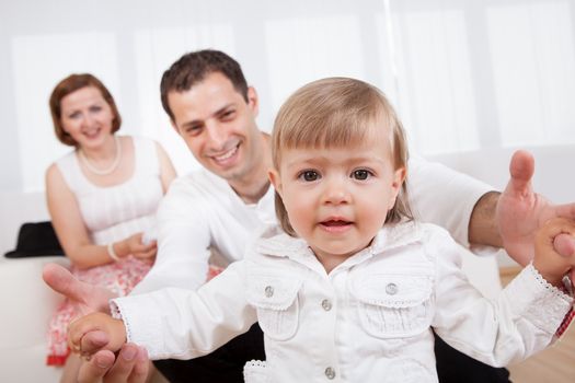 Proud young parents posing sitting on a sofa with their laughing little baby daughter