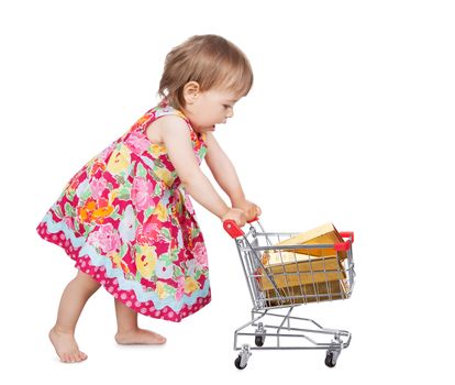 Cute little barefoot girl in a colourful dress pushing a miniature wire shopping trolley isolated on white