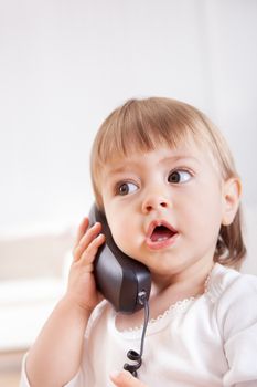 Small girl listening to an old-fashioned handset on a phone with big eyes and her mouth open in awe