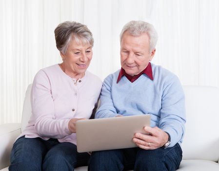 Senior Couple Sitting On Couch And Looking At Laptop Computer