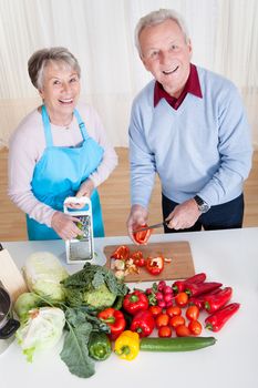 Happy Senior Couple Cutting Vegetables In Kitchen