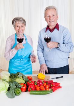 Senior Couple Toasting Wine While Cutting Vegetable In Kitchen