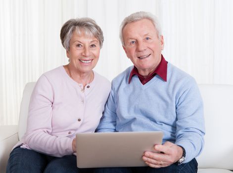 Senior Couple Sitting On Couch And Looking At Laptop Computer