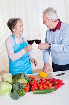 Senior Couple Toasting Wine While Cutting Vegetable In Kitchen