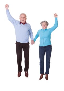 Portrait Of Senior Couple Jumping In Joy Over White Background