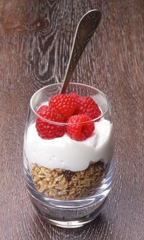 Delicious Dessert with Fresh Ripe Raspberries, Muesli and Dairy Cream in Glass with Silver Dessert Spoon closeup on Wooden background