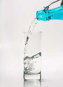 Glass with water pouring from a blue bottle
