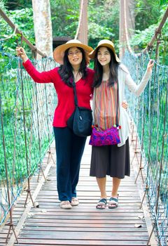 Asian mother and daughter standing together on wooden hanging bridge in forest