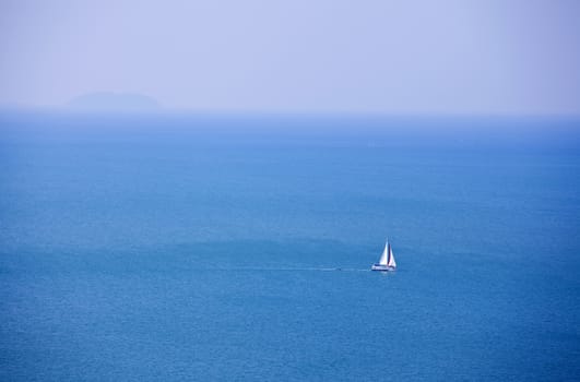 White sailboat sailing on beautiful blue ocean water, near horizon
