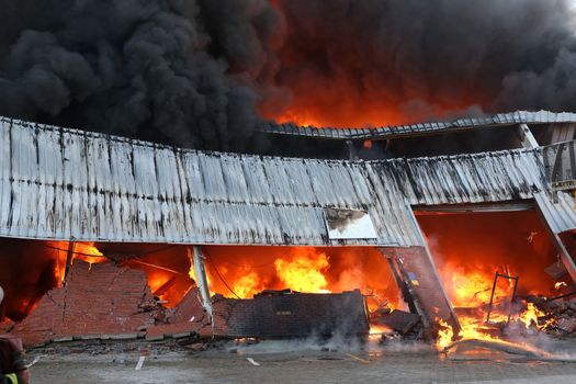 Warehouse building burning with intense flames and fireman attending