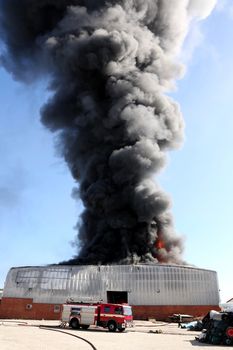 Warehouse building burning with intense flames and fireman attending