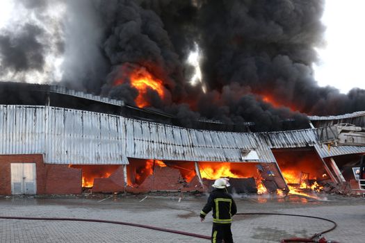 Warehouse building burning with intense flames and fireman attending