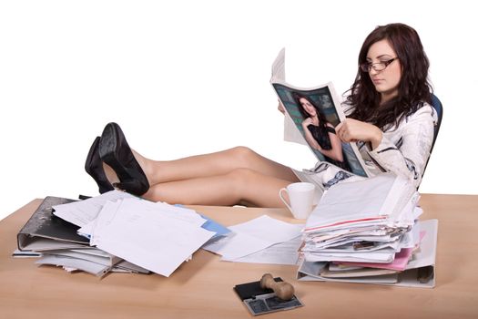 Young female office worker sitting with feet on desk with pile of paper and reads magazine, where she is on the front page