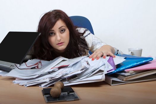 Young female office worker watching helplessly from behind pile of paper