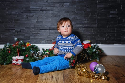 Little boy sitting on the floor surrounded by Christmas decorations