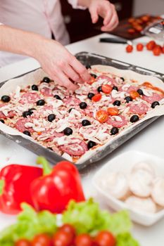 Young man is working on a pizza with pepperoni and mushrooms