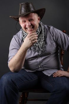 Man in a hat sitting on a chair at dark background