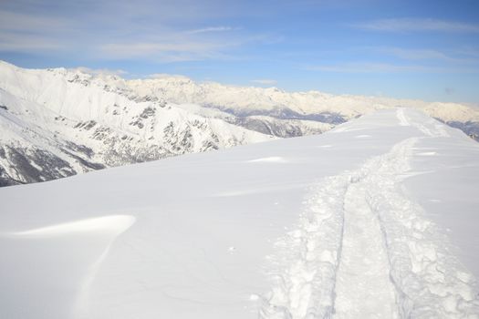 Alpinist hiking uphill by ski touring on the mountain ridge in powder snow with deep track in the foreground and scenic high mountain view in the background