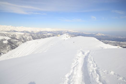 Alpinist hiking uphill by ski touring on the mountain ridge in powder snow with deep track in the foreground and scenic high mountain view in the background