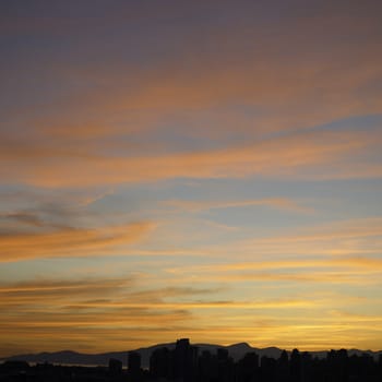 Bright orange sunset over a city, mountains and ocean